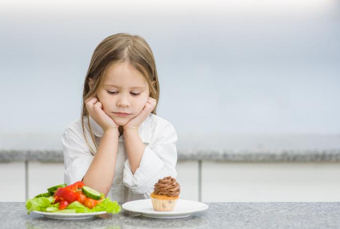 Une petite fille triste choisissant entre des légumes sains et un cupcake : faire des choix alimentaires sains pour une vie équilibrée.